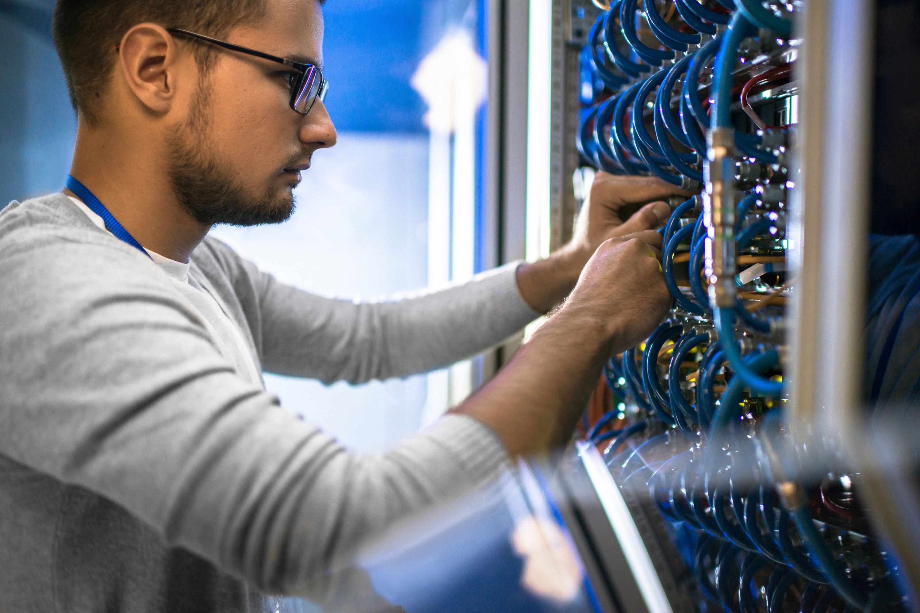 Side view portrait of young man wearing glasses connecting cables in server cabinet while